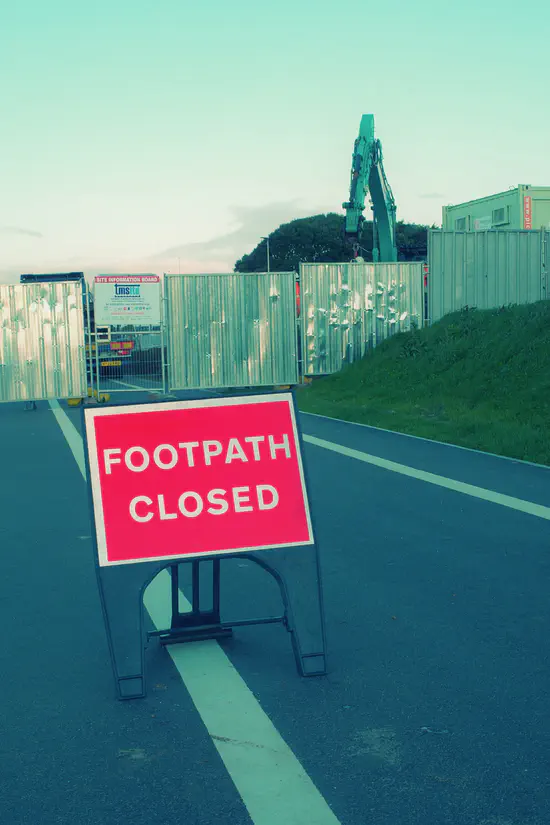 A photograph of Sideshore on Exmouth seafront. The footpath is fenced across with a crane in the background. A sign reads "footpath closed".