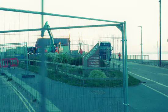 A photograph of Sideshore on Exmouth seafront. Workers in high-visibility jackets and a crane are unpacking the components of the replacement sea wall.