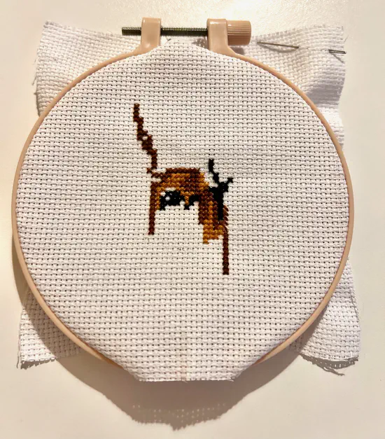 A photograph of a cross stitch in progress. The centre of the piece has a handful of black and brown patterns.