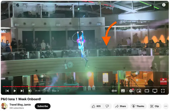 A screenshot of a YouTube video uploaded by Travel Blog Jamie. A live acrobatic show is being performed onboard a cruise ship. An orange arrow is painted on to point me out in the audience.